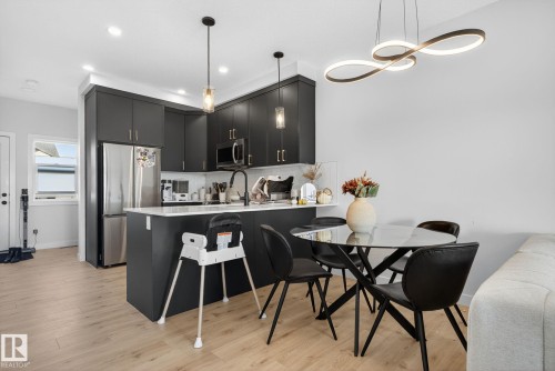 Kitchen with a peninsula, a kitchen bar, stainless steel appliances, dark cabinets, and light wood-type flooring - 382 Crystallina Nera Drive, Edmonton, AB - Indoor