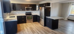 Kitchen featuring appliances with stainless steel finishes, decorative backsplash, light wood-type flooring, and light stone counters - 