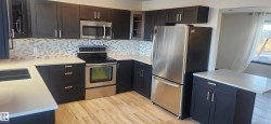 Kitchen with stainless steel appliances, decorative backsplash, light wood finished floors, light stone counters, and glass insert cabinets - 