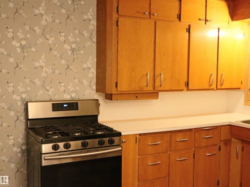 Kitchen with gas range, wallpapered walls, light countertops, and brown cabinetry - 4032A Twp Rd 604, Rural Barrhead County, AB - Indoor Photo Showing Kitchen