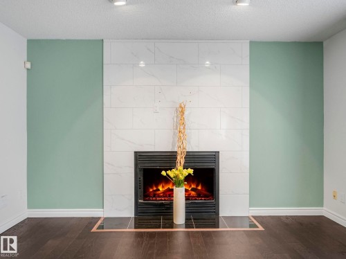 Detailed view of wood finished floors, a textured ceiling, and a tiled fireplace - 316 Burton Road, Edmonton, AB - Indoor With Fireplace