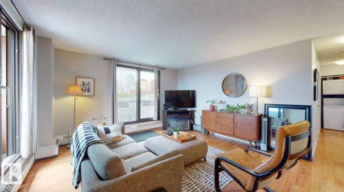 Living room featuring a textured ceiling, light wood-style flooring, and a baseboard heating unit - 301 10175 109 Street, Edmonton, AB - Indoor Photo Showing Living Room
