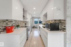 Kitchen with modern cabinets, white cabinetry, stainless steel appliances, backsplash, and wall chimney range hood - 