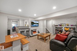 Living room featuring a brick fireplace, light colored carpet, stairway, recessed lighting, and brick wall - 