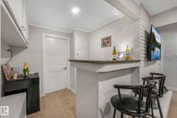Indoor dry bar with ornamental molding, white cabinets, light colored carpet, and wooden walls - 