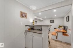Kitchen with dark countertops, white cabinetry, light carpet, a kitchen breakfast bar, and a peninsula - 