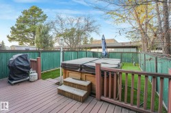 Wooden terrace featuring area for grilling, a fenced backyard, and a hot tub - 