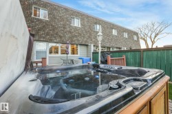 Back of house with a hot tub, a deck, and mansard roof - 