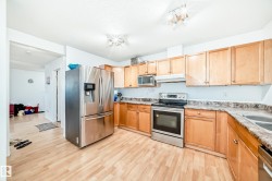 Kitchen with stainless steel appliances, light wood-style flooring, light brown cabinetry, and under cabinet range hood - 