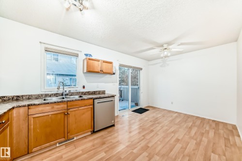 Kitchen with light wood-style floors, stainless steel dishwasher, a textured ceiling, dark countertops, and ceiling fan - #48 - 2503 24 Street Nw, Edmonton, AB - Indoor Photo Showing Kitchen With Double Sink