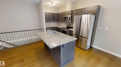 Kitchen featuring dark brown cabinets, appliances with stainless steel finishes, a center island with sink, light stone counters, and dark wood-style flooring - 