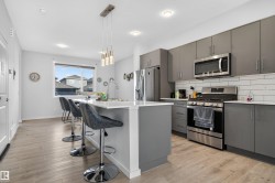 Kitchen featuring gray cabinets, stainless steel appliances, decorative backsplash, a center island with sink, and a breakfast bar - 
