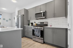 Kitchen featuring gray cabinets, appliances with stainless steel finishes, tasteful backsplash, light wood-style floors, and modern cabinets - 