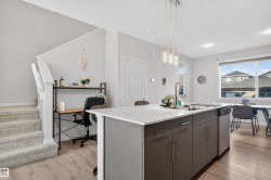 Kitchen with hanging light fixtures, a center island with sink, light wood-style floors, and dark brown cabinets - 