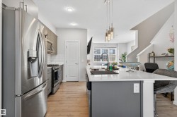 Kitchen featuring appliances with stainless steel finishes, gray cabinets, decorative light fixtures, an island with sink, and a breakfast bar area - 