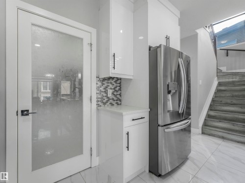 Kitchen with white cabinets, stainless steel fridge, backsplash, light marble finish flooring, and modern cabinets - 2412 14 Avenue, Edmonton, AB - Indoor