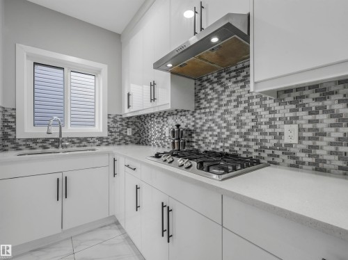 Kitchen with decorative backsplash, white cabinetry, extractor fan, and light marble finish floors - 2412 14 Avenue, Edmonton, AB - Indoor Photo Showing Kitchen With Upgraded Kitchen