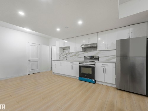 Kitchen with stainless steel appliances, white cabinets, decorative backsplash, light wood-type flooring, and under cabinet range hood - 2412 14 Avenue, Edmonton, AB - Indoor Photo Showing Kitchen With Upgraded Kitchen