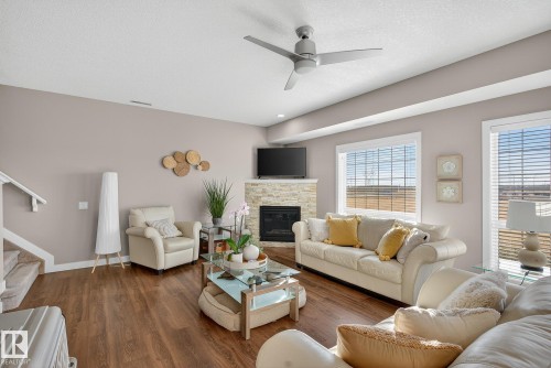 Living room featuring a stone fireplace, wood finished floors, stairs, a textured ceiling, and ceiling fan - 117 7293 South Terwillegar Drive, Edmonton, AB - Indoor Photo Showing Living Room With Fireplace