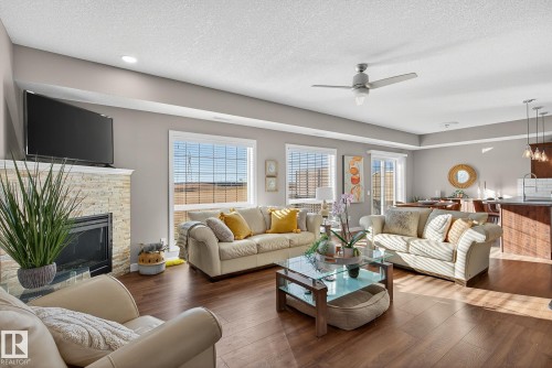 Living room with a textured ceiling, hardwood / wood-style flooring, a ceiling fan, and a glass covered fireplace - 117 7293 South Terwillegar Drive, Edmonton, AB - Indoor Photo Showing Living Room With Fireplace