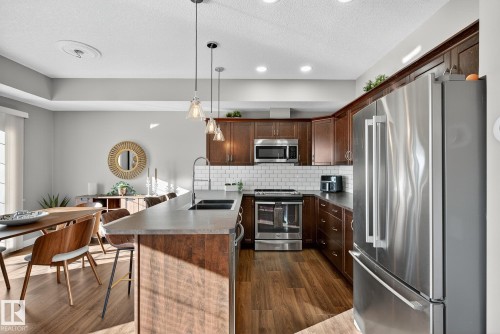 Kitchen featuring stainless steel appliances, a peninsula, backsplash, a textured ceiling, and a kitchen bar - 117 7293 South Terwillegar Drive, Edmonton, AB - Indoor Photo Showing Kitchen With Double Sink With Upgraded Kitchen