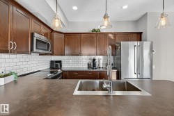 Kitchen featuring dark countertops, appliances with stainless steel finishes, backsplash, hanging light fixtures, and a textured ceiling - 