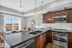 Kitchen with appliances with stainless steel finishes, decorative light fixtures, dark countertops, dark wood-style floors, and tasteful backsplash - 