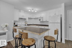 Kitchen featuring white appliances, a kitchen breakfast bar, a kitchen island, backsplash, and white cabinets - 