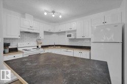Kitchen featuring white appliances, white cabinets, dark countertops, under cabinet range hood, and a textured ceiling - 