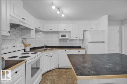 Kitchen with white appliances, dark countertops, decorative backsplash, under cabinet range hood, and a textured ceiling - 