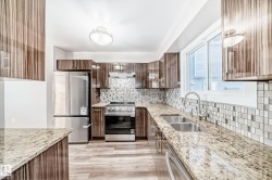 Kitchen featuring backsplash, light stone countertops, appliances with stainless steel finishes, under cabinet range hood, and light wood-style flooring - 