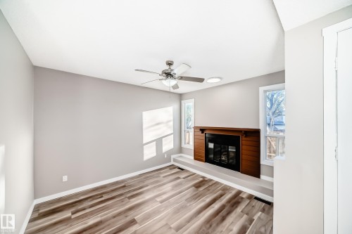 Unfurnished living room with a glass covered fireplace, wood finished floors, and a ceiling fan - 44 4403 Riverbend Road, Edmonton, AB - Indoor With Fireplace