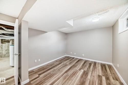 Finished basement featuring light wood-type flooring, a textured ceiling, and water heater - 44 4403 Riverbend Road, Edmonton, AB - Indoor Photo Showing Other Room