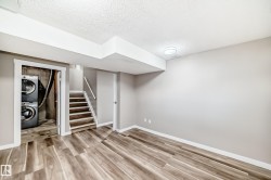 Finished basement with a textured ceiling, stairs, light wood-style floors, and estacked washer and dryer - 