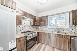 Kitchen with stainless steel appliances, light stone countertops, under cabinet range hood, and light wood-style floors - 