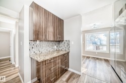 Bar with freestanding refrigerator, light stone countertops, light wood finished floors, decorative backsplash, and modern cabinets - 