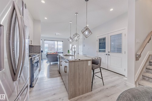 Kitchen with stainless steel appliances, a center island with sink, tasteful backsplash, decorative light fixtures, and light wood-style flooring - 8086 Kiriak Link, Edmonton, AB - Indoor Photo Showing Kitchen With Stainless Steel Kitchen With Upgraded Kitchen