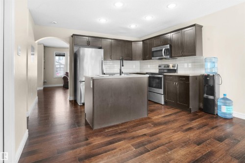 Kitchen with stainless steel appliances, light countertops, arched walkways, dark brown cabinetry, and backsplash - 1442 33A Street Nw, Edmonton, AB - Indoor Photo Showing Kitchen