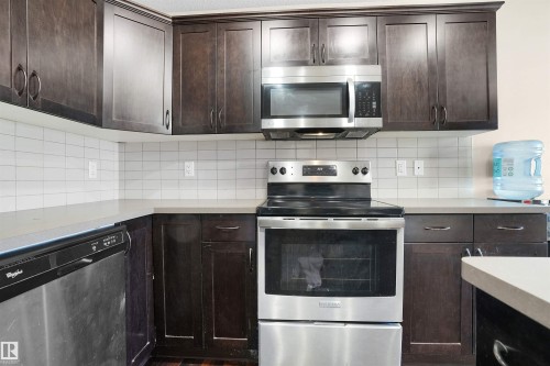 Kitchen with stainless steel appliances, dark brown cabinetry, light countertops, and backsplash - 1442 33A Street Nw, Edmonton, AB - Indoor Photo Showing Kitchen With Upgraded Kitchen