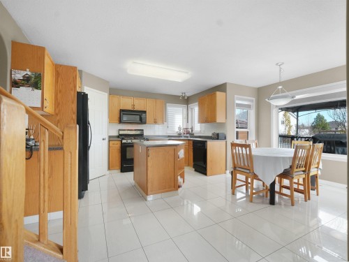 Kitchen with a kitchen island, black appliances, light tile patterned flooring, pendant lighting, and dark countertops - 94 Dechene Road, Edmonton, AB - Indoor
