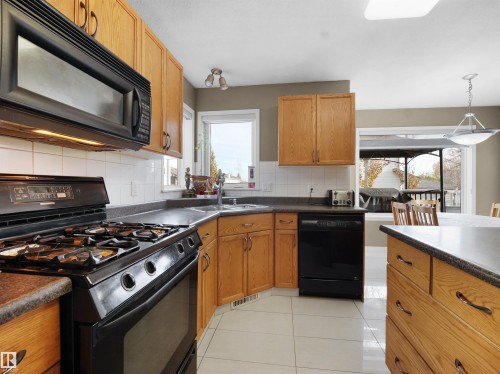 Kitchen featuring black appliances, dark countertops, tasteful backsplash, light tile patterned flooring, and brown cabinetry - 94 Dechene Road, Edmonton, AB - Indoor Photo Showing Kitchen With Double Sink