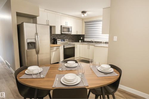 Kitchen with appliances with stainless steel finishes, decorative backsplash, white cabinetry, and light wood-type flooring - 4203 83 Street, Edmonton, AB - Indoor