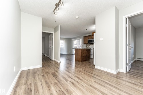 Unfurnished living room featuring a textured ceiling, light wood-style flooring, rail lighting, and a baseboard heating unit - 108 2305 35A Avenue, Edmonton, AB - Indoor