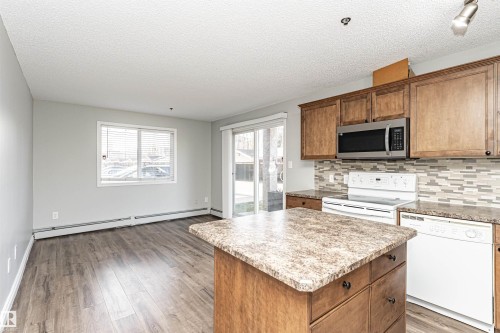 Kitchen featuring brown cabinetry, white appliances, a center island, a textured ceiling, and decorative backsplash - 108 2305 35A Avenue, Edmonton, AB - Indoor Photo Showing Kitchen