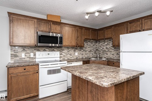 Kitchen with white appliances, a center island, a textured ceiling, tasteful backsplash, and dark wood-type flooring - 108 2305 35A Avenue, Edmonton, AB - Indoor Photo Showing Kitchen