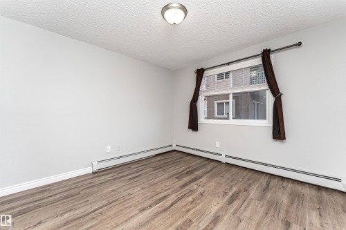 Unfurnished room with a textured ceiling, wood finished floors, and a baseboard heating unit - 108 2305 35A Avenue, Edmonton, AB - Indoor Photo Showing Other Room