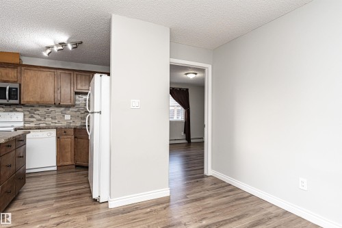 Kitchen featuring a textured ceiling, white appliances, decorative backsplash, light wood finished floors, and brown cabinetry - 108 2305 35A Avenue, Edmonton, AB - Indoor Photo Showing Kitchen