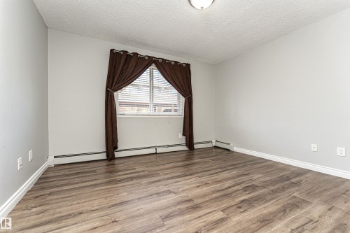 Spare room featuring wood finished floors, a textured ceiling, and a baseboard heating unit - 108 2305 35A Avenue, Edmonton, AB - Indoor Photo Showing Other Room
