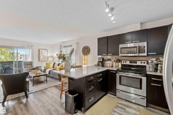 Kitchen featuring appliances with stainless steel finishes, light stone countertops, a peninsula, a textured ceiling, and light wood-style flooring - 