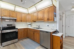 Kitchen with stainless steel appliances, backsplash, light countertops, light wood-style flooring, and brown cabinetry - 